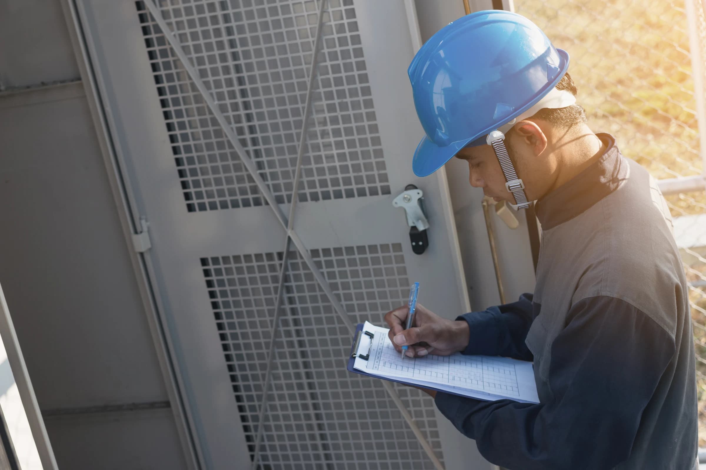 An inspector in a hard hat writing intake details on a clipboard