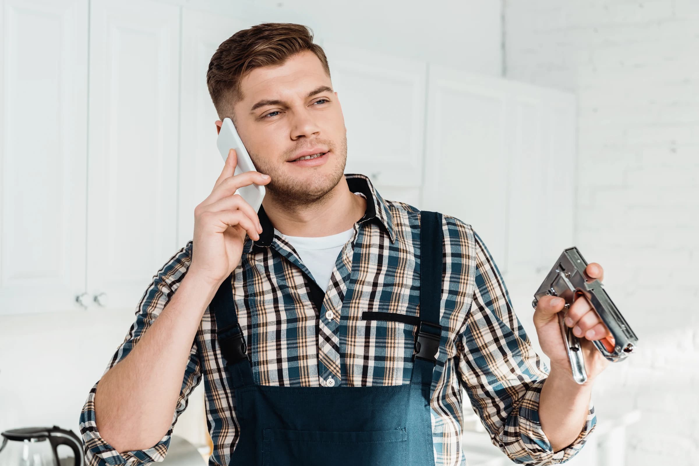 A repairman talking on the phone while holding a staple gun