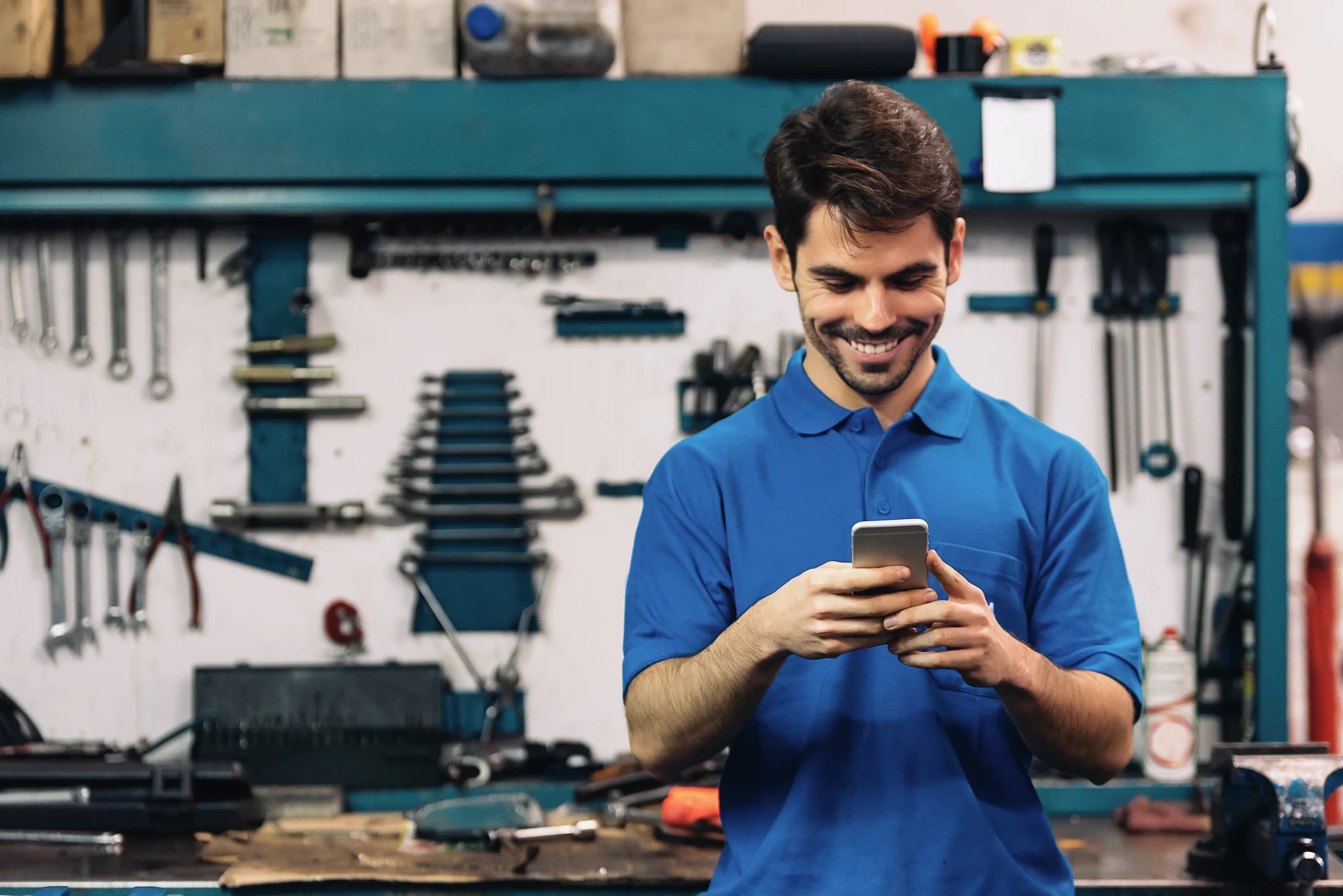 A smiling man using his smartphone in an automotive repair shop