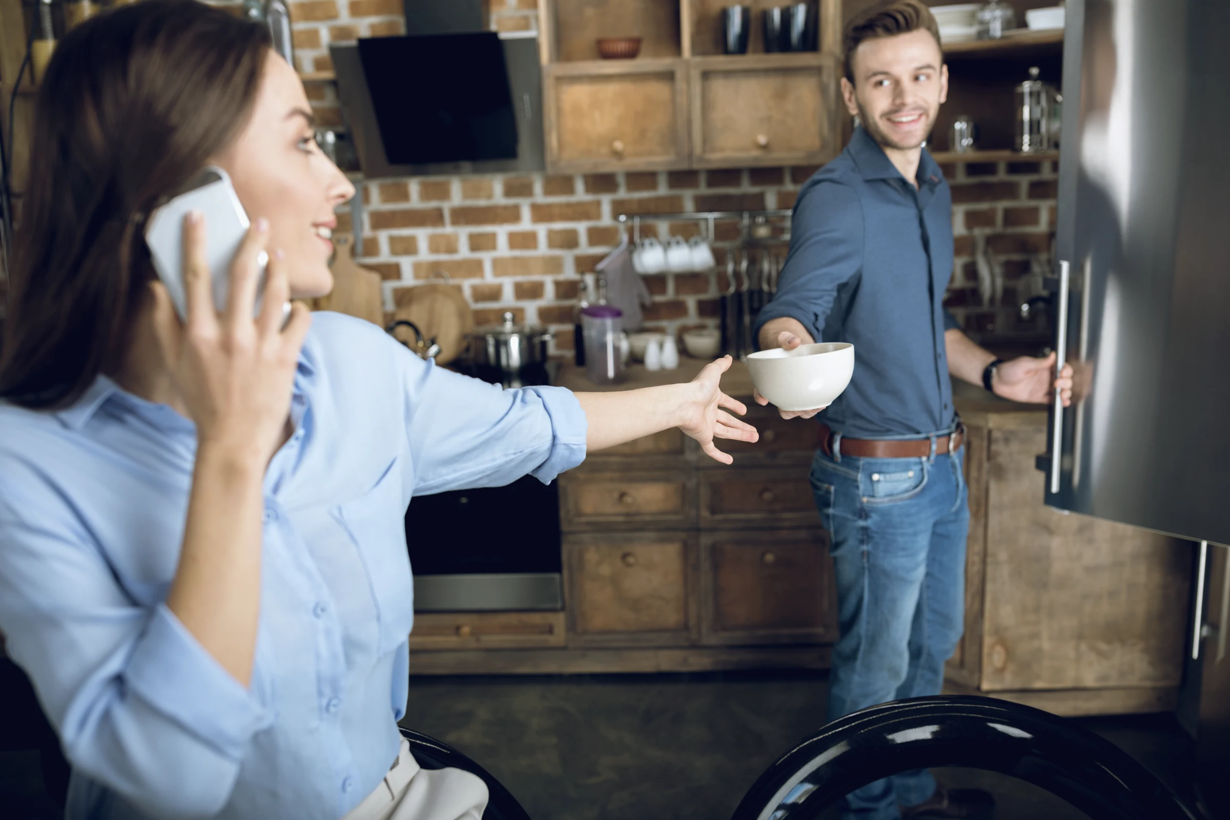 A woman talking on the phone in a kitchen with a man beside her