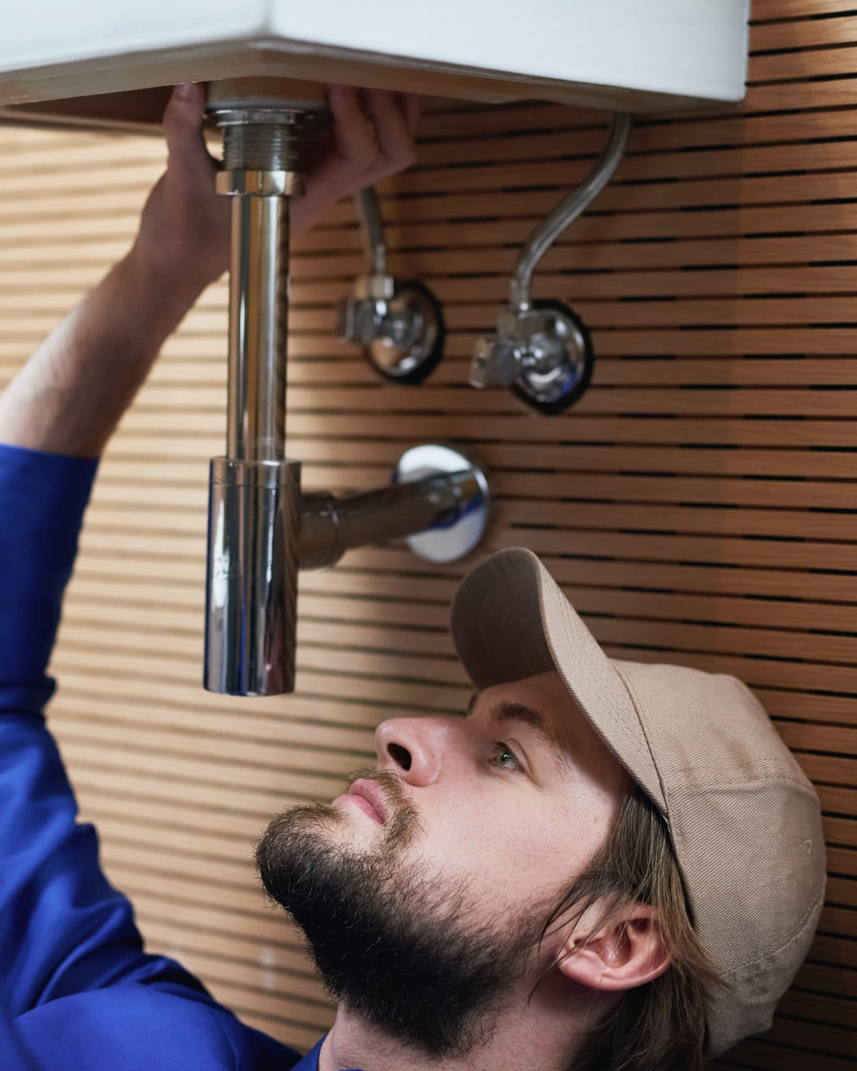 A plumber on his back under a sink, both hands on a wrench.