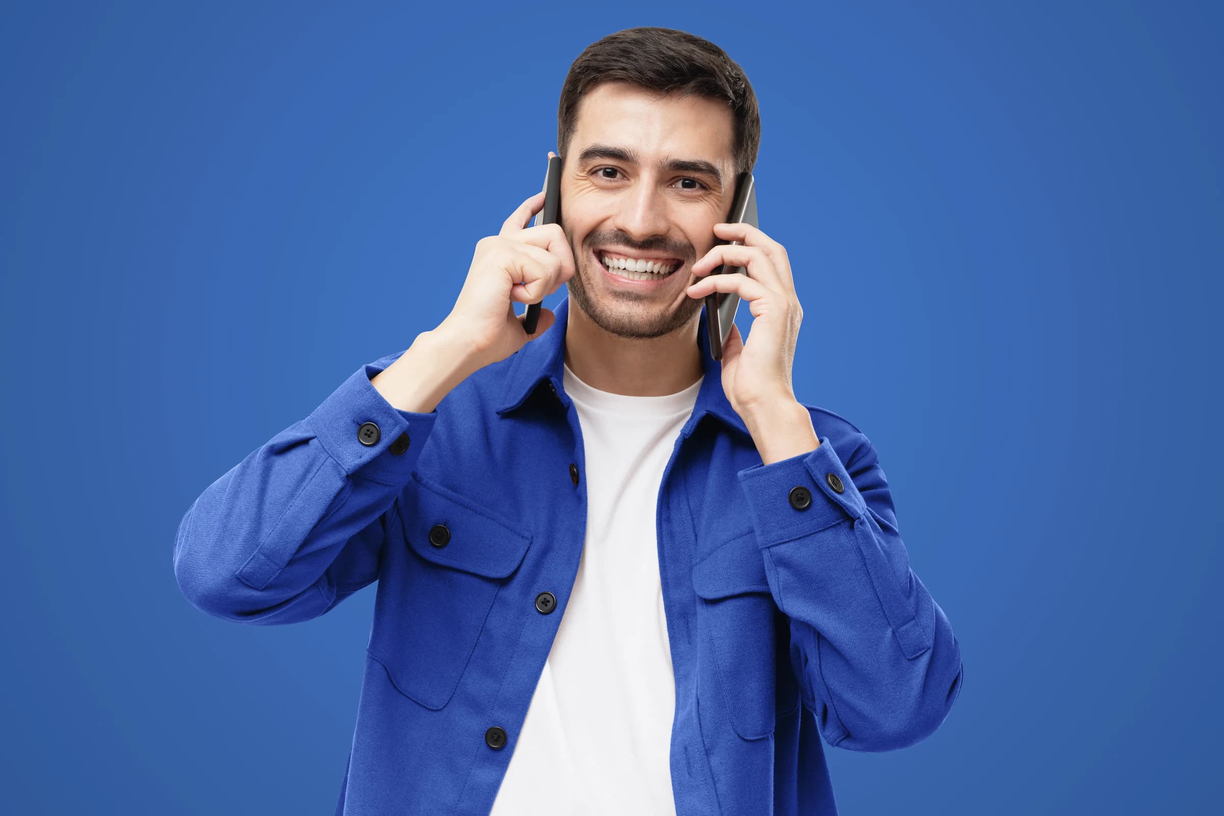 A man using two cellphones against a blue backdrop