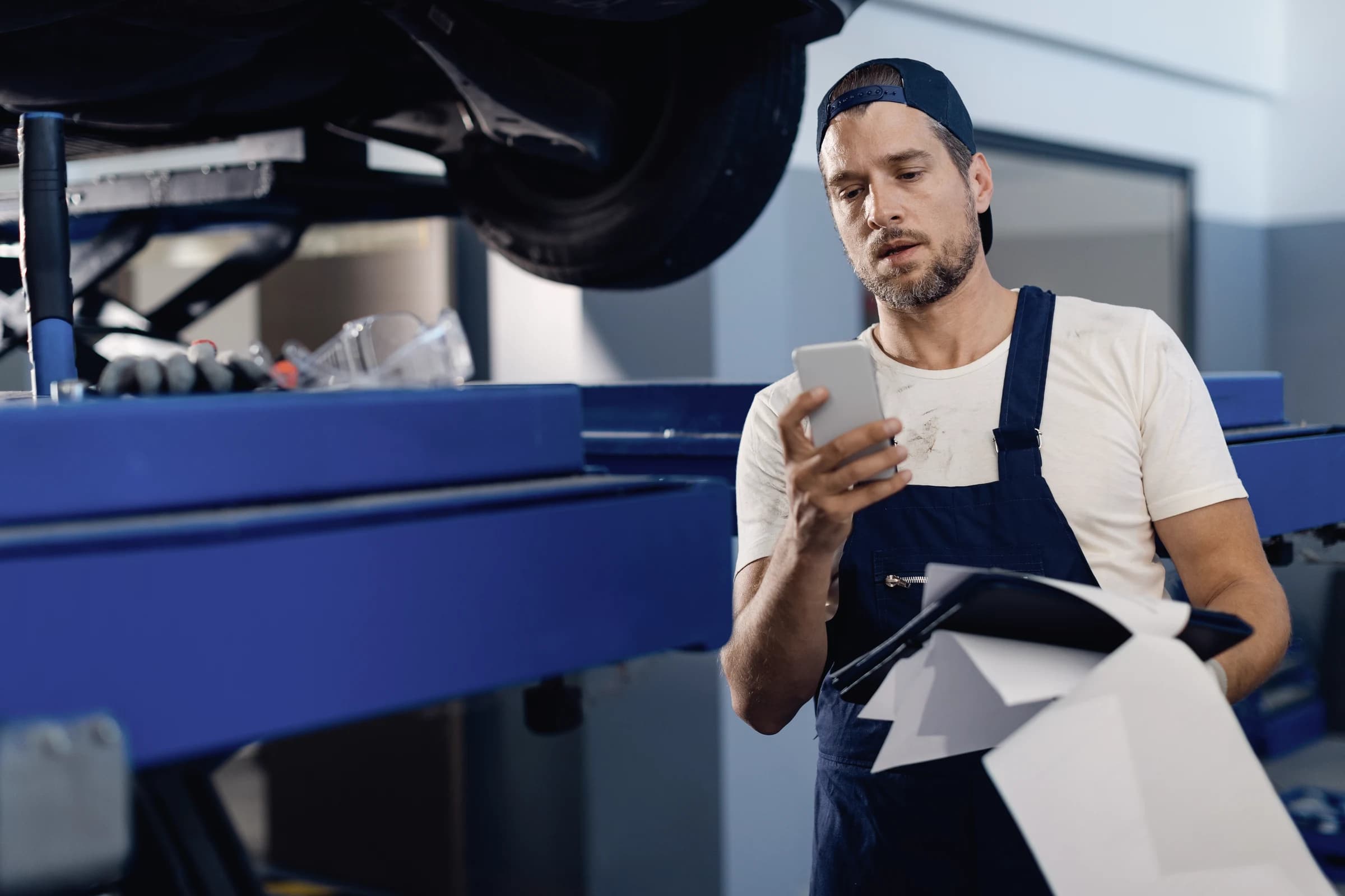 A mechanic using a smartphone in an auto repair shop