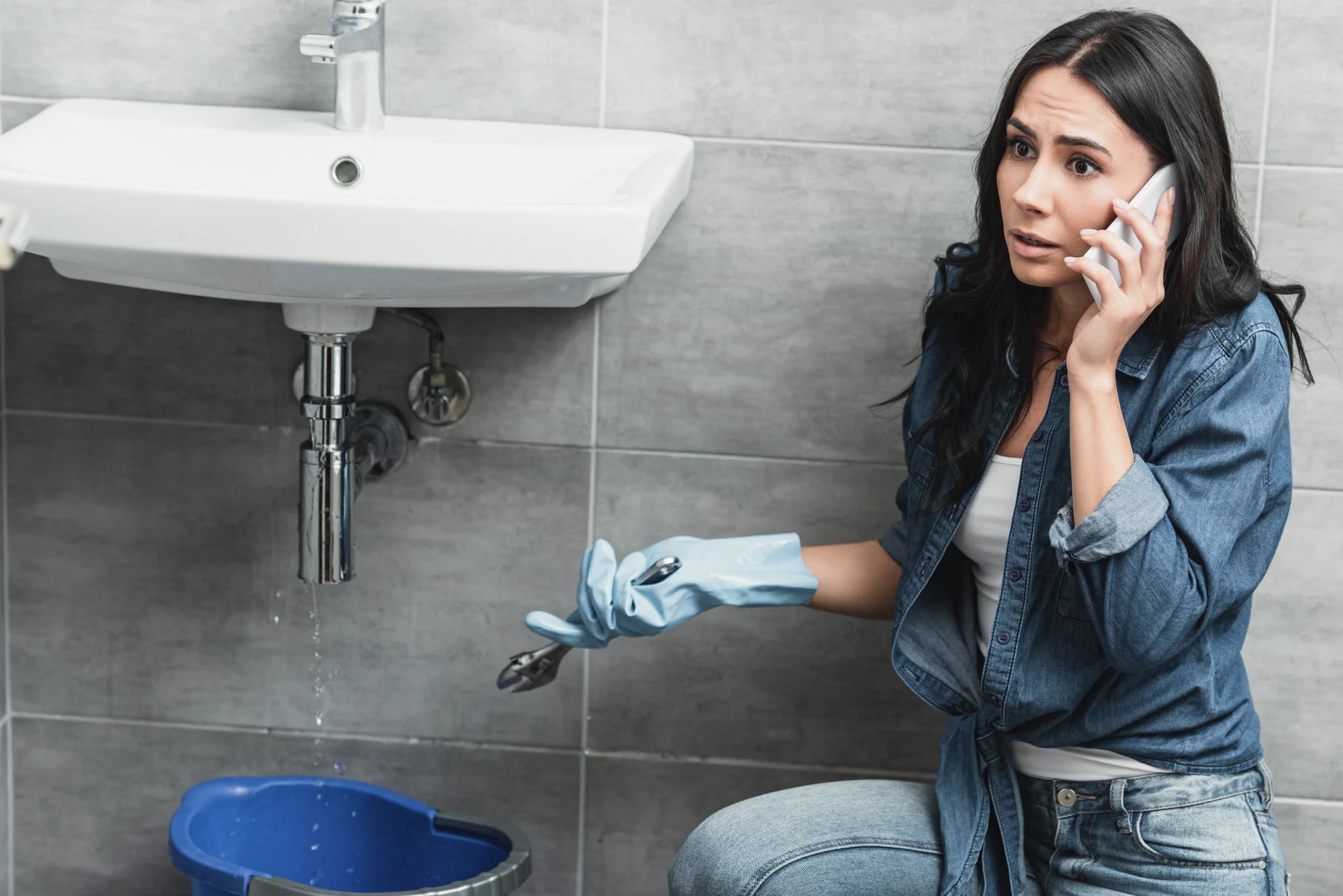 A tenant on the phone kneeling by a leaking sink.